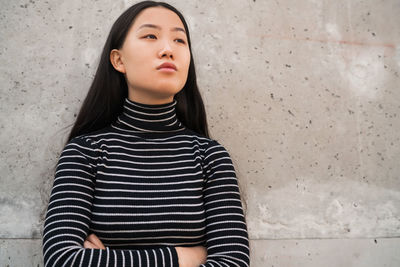 Young woman looking away while standing against wall