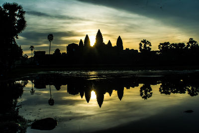 Silhouette of temple by lake against sky during sunset