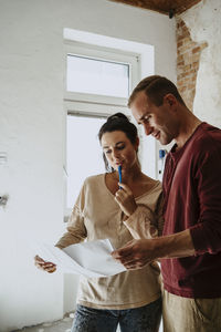 Couple discussing over floor plan in room while renovating home