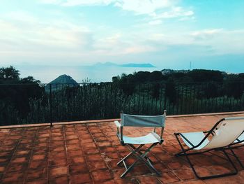 Empty chairs and tables by swimming pool against sky
