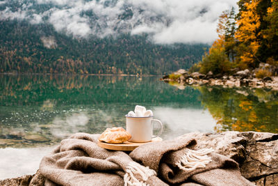 Picnic with cacao on stones near lake and autumn forest in the bavarian mountains, germany