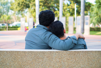 Rear view of couple sitting on retaining wall