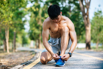 Full length of shirtless man sitting on tree