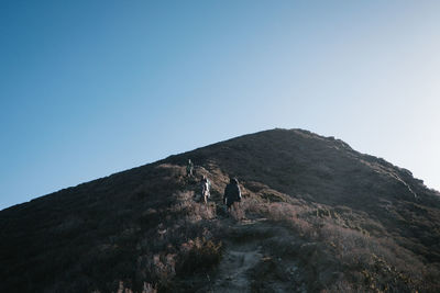 Low angle view of people on mountain against clear blue sky