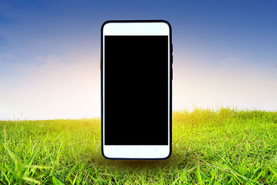 Digital composite image of mobile phone on grassy field against sky