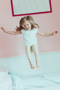 Cheerful girl jumping on bed at home