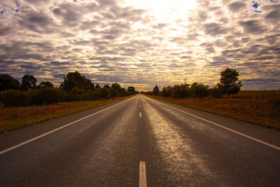 Road by trees against sky during sunset