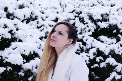 Woman looking away against snowy plants during winter