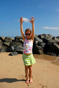 Portrait of girl with arms raised standing at beach against sky