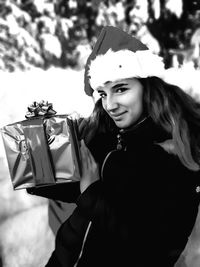 Portrait of smiling young woman holding christmas present while standing outdoors