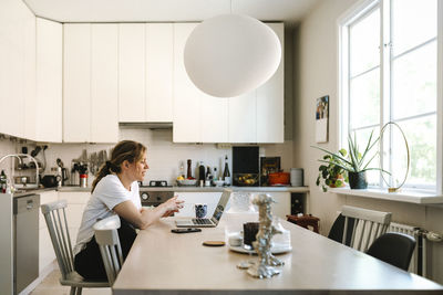 Female freelancer discussing on video call through laptop in kitchen at home