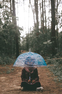 Midsection of woman with umbrella in forest during rainy season