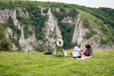 Rear view of woman feeding a baby on grassy field in mountains