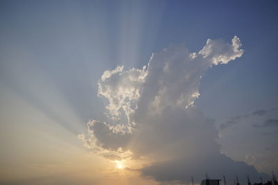 Low angle view of sunlight streaming through clouds during sunset