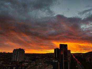 Buildings in city against dramatic sky during sunset