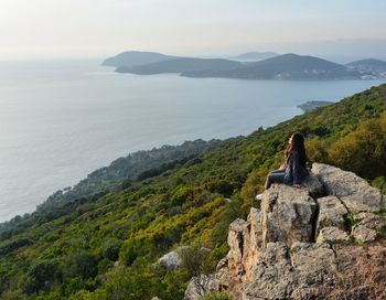 Man sitting on rock by sea against sky