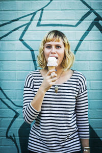 Portrait of woman eating ice cream while standing against wall