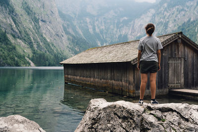 Rear view of teenage girl standing on rock by lake against mountains