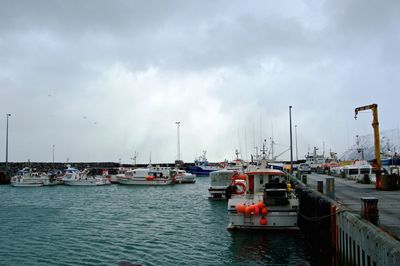 Boats in harbor against cloudy sky