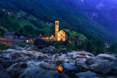 Illuminated buildings by mountain against trees and mountains