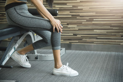 Low section of woman touching knee while sitting in gym