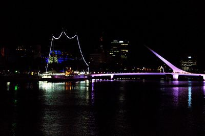 Illuminated bridge over river in city at night