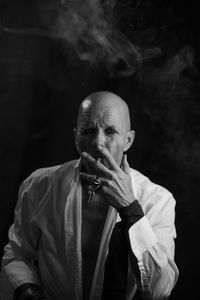 Portrait of man smoking cigarette against black background