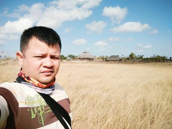 Portrait of mid adult man standing on field against cloudy sky during sunny day