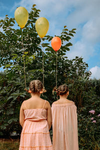 Two sisters in pink dresses are on the street. balloons are tied to their braided hair