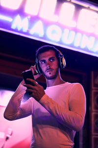 Man with a smartphone listening music at night. color lights