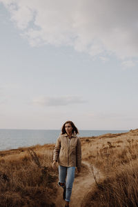 Young woman walking on dirt road against sea and sky