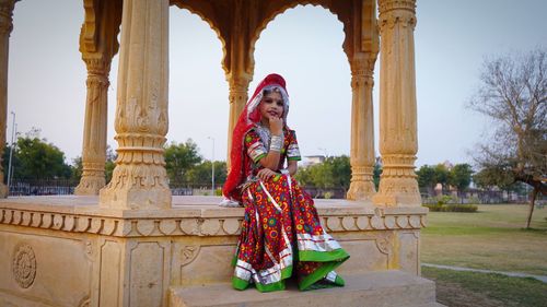 Portrait of smiling young girl sitting against historical building