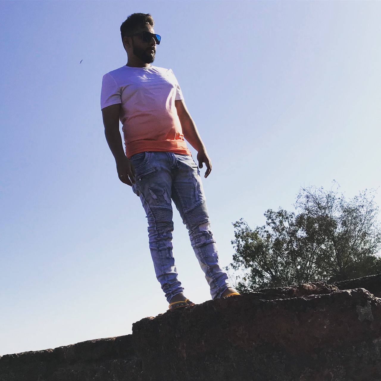 LOW ANGLE VIEW OF YOUNG MAN STANDING AGAINST CLEAR SKY