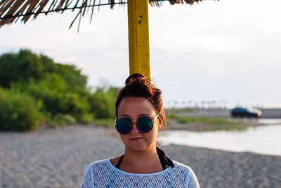 Portrait of young woman wearing sunglasses standing at beach