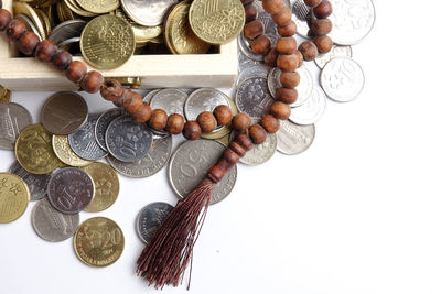 Directly above shot of rosary beads with coins in wooden box on white background