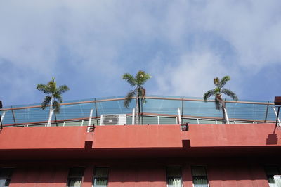 Low angle view of palm trees on building patio against cloudy sky