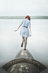 Rear view of woman standing on pipeline at sea