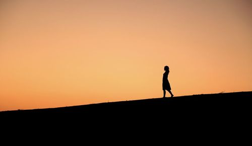Silhouette woman walking on landscape against sunset sky