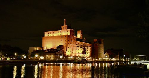 Illuminated buildings by river against sky at night