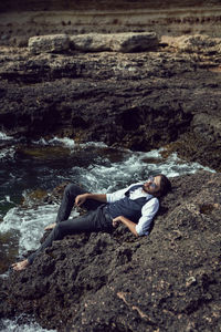 Man with a beard in dark clothes and a white shirt sits on the stone seashore in  crimea tarkhankut