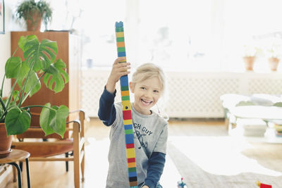 Happy girl holding tower made of toy blocks at home