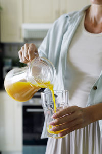 Hands of woman pouring orange juice in glass from jug