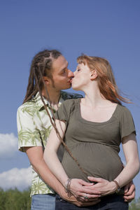 Low angle view of man kissing woman against sky