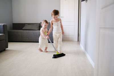 Children siblings with mop sweep floor in bright living room, help with housework and relationships