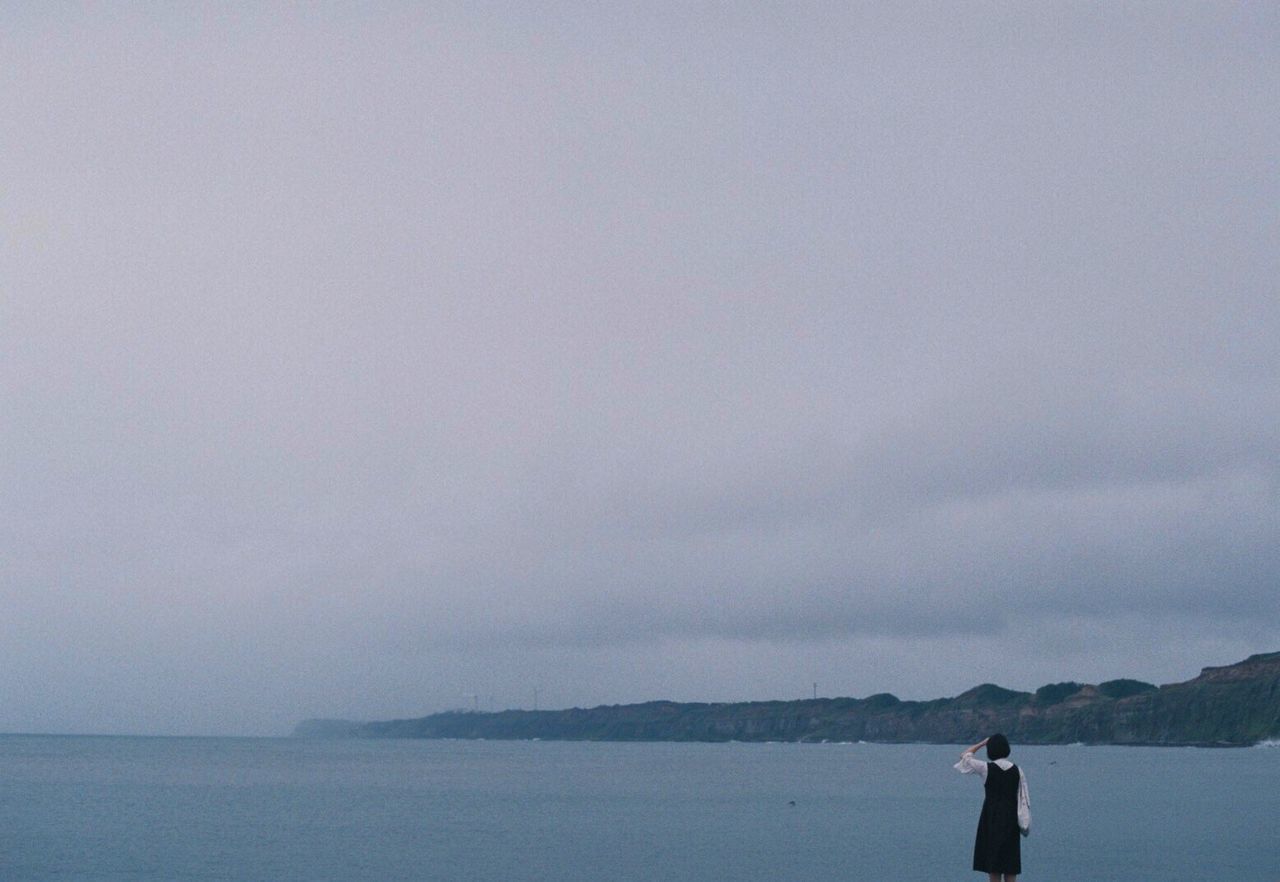 REAR VIEW OF A WOMAN PHOTOGRAPHING SEA