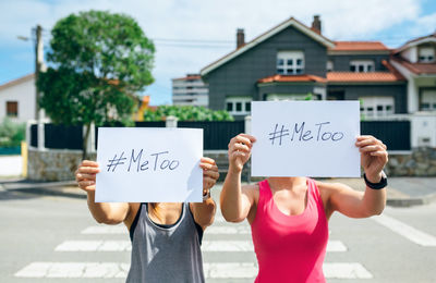 Women covering face with placard while standing on city street