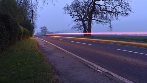 Empty road by trees against sky