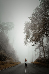 Rear view of woman standing on road during foggy weather against sky
