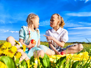 Happy friends sitting on field against sky