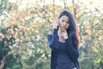 Young woman talking on mobile phone while standing against trees